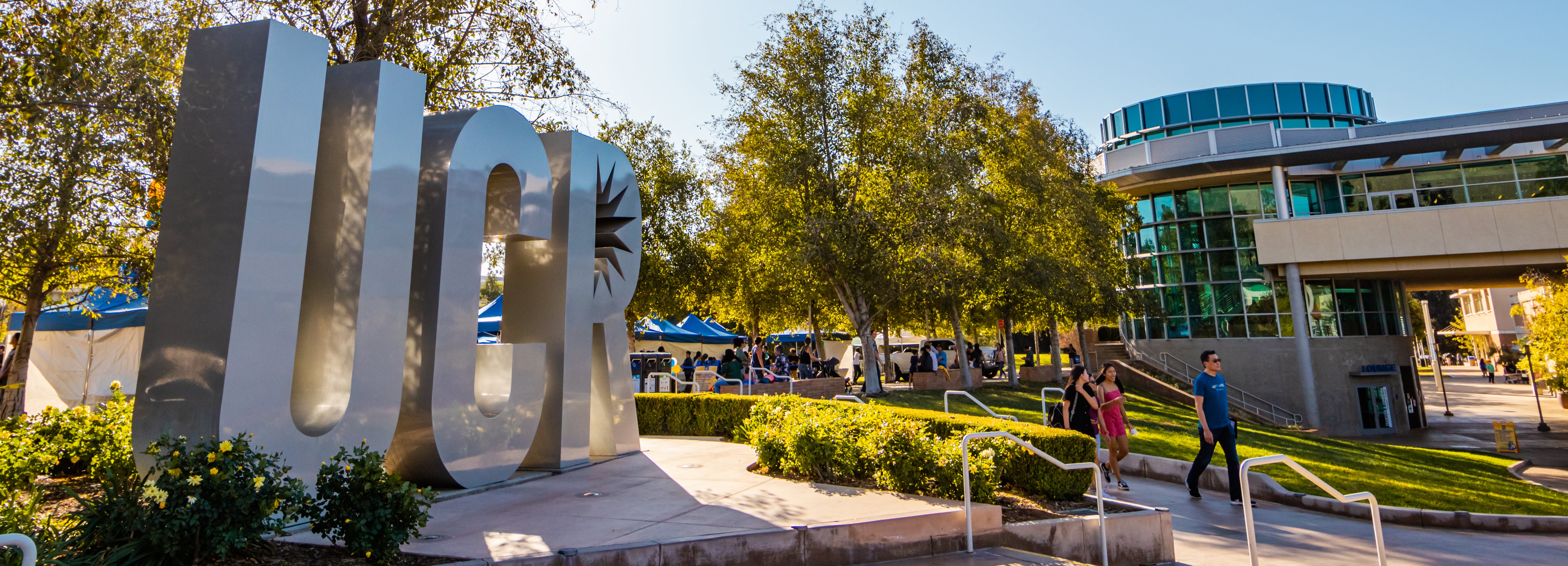 A photo of the letters U C and R on campus surrounded be trees and buildings