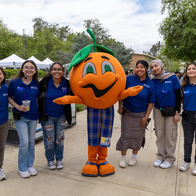 A mascot of an orange poses with a group of students 